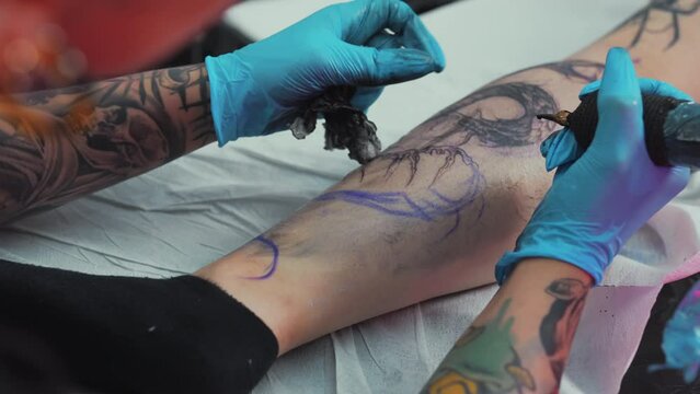 Tattoo artist making tattoo on girl leg in salon tattoo making process in studio. High quality 4k footage