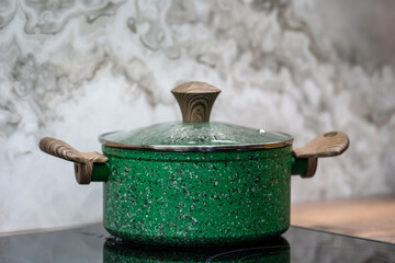 Granite frying pan with glass on black induction stove against grey wall. Cooking pot.