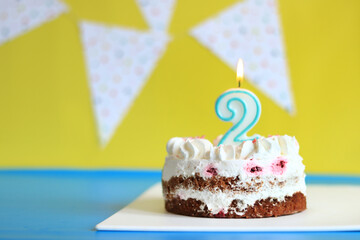 Celebration cake with a lit birthday candle. Cake for the second birthday. Cake on a festive background with birthday flags. Happy birthday