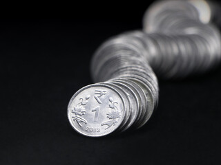 1 (one) rupee coins of india made of silver stacked together in a curved row shaped like a snake in closeup isolated in a black background