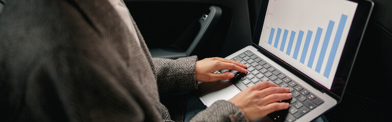 Professional woman analyst working on laptop sitting car leather backseat on the way to office