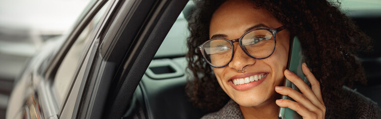 Smiling businesswoman talking by phone with client while sitting on back seat in car