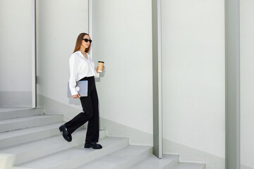 An office employee in a white shirt and trousers is walking up the stairs with a laptop. Street concept