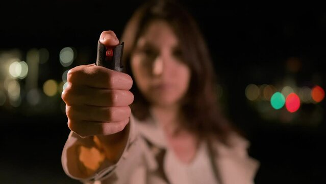 Confident young woman alone in the city at night pointing a pepper spray directly at the camera, blur and replay action