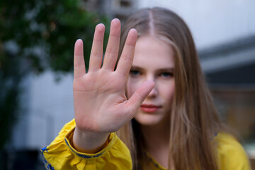 beautiful young woman in yellow shirt shows palm forward stop stop war in ukraine aggressor invasion violence. against racial gender discrimination. Determined European woman makes a protest sign