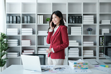 Beautiful asian businesswoman working on laptop and talking the phone. Successful business results in modern office wear red shirt.