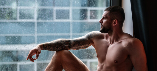 Man window on rainy weather looking through the window with rain drops, autumn banner. Handsome...