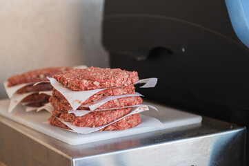 beef patties for hamburgers  are stacked with a baking paper divider near the gas grill in the backyard of a country house. Interesting pastime with family and friends.