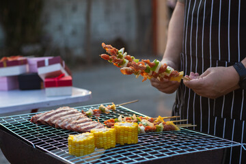 Meat and skewers ingredients for barbecue party are placed on grill to cook barbecue and make it ready for family to join barbecue party tonight.  party background image has Copy Space for text.
