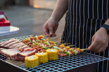 Meat and skewers ingredients for barbecue party are placed on grill to cook barbecue and make it ready for family to join barbecue party tonight.  party background image has Copy Space for text.