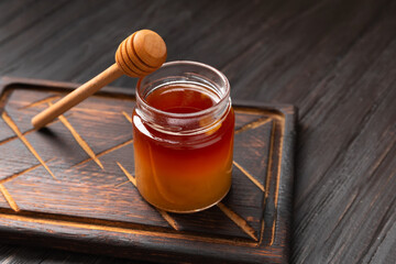 Buckwheat honey in a jar and a dipper on a dark wooden board.