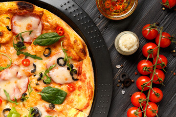 Pizza on a black baking dish on a dark wooden background, top view.