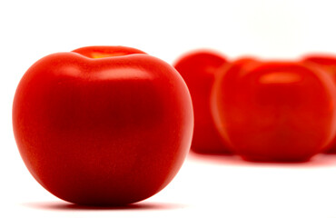 Fresh and ripe tomato with defocused tomatoes in the background. Isolated on white background with copy space. Close-up view.