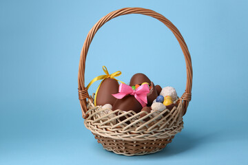 Wicker basket with tasty chocolate Easter eggs and different candies on light blue background