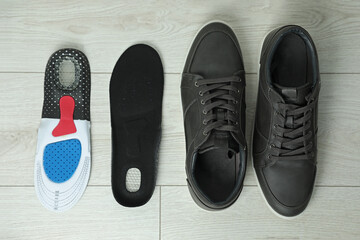Orthopedic insoles near shoes on floor, flat lay