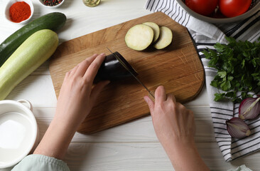 Cooking delicious ratatouille. Woman cutting fresh eggplant at white wooden table, top view