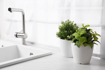 Fototapeta na wymiar Artificial potted herbs on white marble countertop near sink in kitchen. Home decor