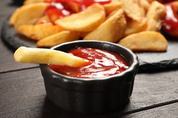 Delicious french fry with tasty ketchup on dark wooden table, closeup