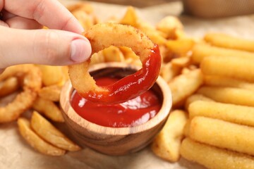 Woman dipping onion ring into bowl with tasty ketchup at table, closeup