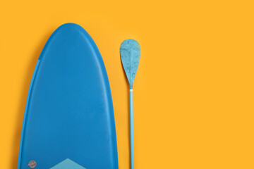SUP board and paddle on yellow background, flat lay with space for text. Water sport