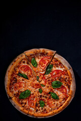 Delicious fragrant pizza-Margherita with mozzarella, tomatoes and basil on tomato sauce on black background