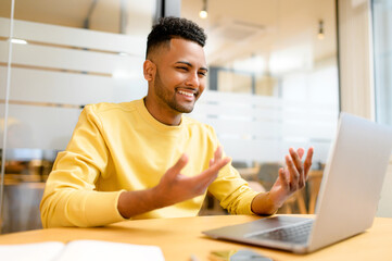 Young Indian man holding video call, waving, greeting participants online, male student taking online classes, involved virtual meeting, talking and gesturing