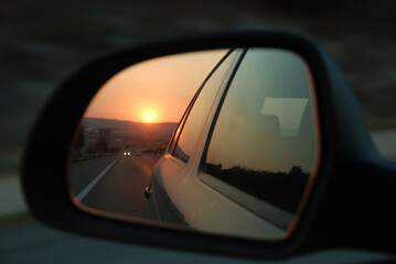 sunset in the side mirror of a car on the road