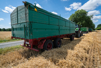 Fototapeta premium Trecker und Ladewagen warten bei der Getreideernte am Feldrand.