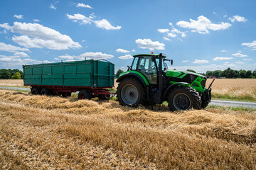 Trecker und Ladewagen warten bei der Getreideernte am Feldrand.