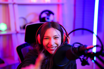 Asian young esport woman cheerful and pointing finger portrait with camera after stream playing game online and use technology gadget for communication in entertainment room