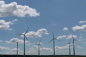 Silhouette von Windkraftanlagen vor blauem Himmel mit weißen Wolken.