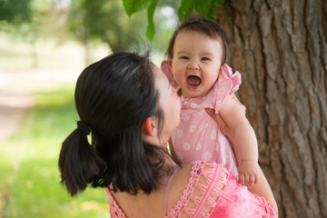 Asian mum and little child - young happy and beautiful Korean woman playing on city park with adorable and cheerful baby girl in mother and daughter love and bonding