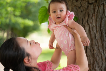 Asian mum and little child - young happy and beautiful Korean woman playing on city park with adorable and cheerful baby girl in mother and daughter love and bonding