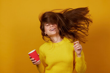The girl holds a disposable glass in her hand and rejoices on a yellow background