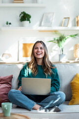 Beautiful kind woman working with laptop while sitting on couch in living room at home