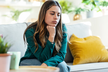 Beautiful young woman thinking and worried sitting on couch at home.