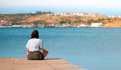 Woman relaxing meditating on the pier by the sea, enjoying her day.