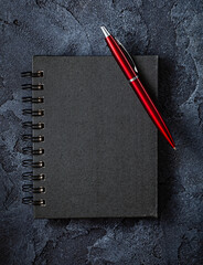 Black Notepad With Red Ballpoint Pen On Stone Background