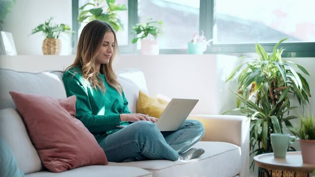 Video of beautiful kind woman working with laptop while sitting on couch in living room at home