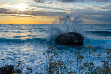 A seascape of waves crushing over a rock during sunset.