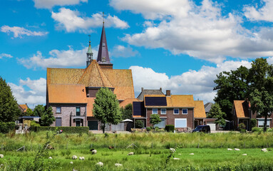 Fototapeta na wymiar Beautiful green dutch sheep pasture, sleepy rural idyllic countryside village with church tower - Oud Bergen (Limburg), Netherlands