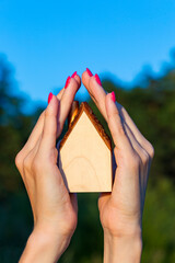 Woman hands carefully holding a wooden house model. Concept of home protection, care and insurance