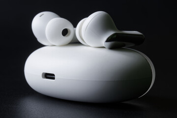White tws headphones with an oval white charging case on a black background. Photo. Selective...