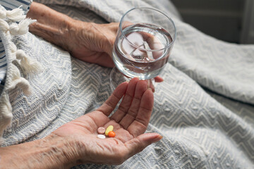 Old woman holding medicine and a glass of water. Colorful pills in old woman hand. Care for the...