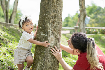 little latin girl playing happily with her mother around a tree in the park, smiling and spending the afternoon together.