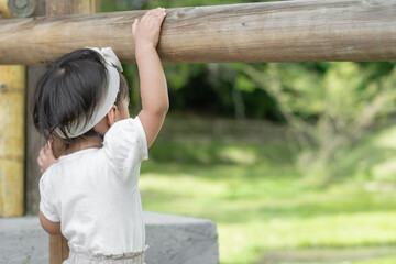 view of the back of a little latin girl standing next to the wooden fence admiring nature