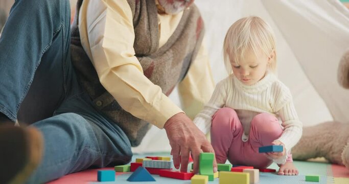 Building blocks, playful and senior man with his grandchild in her playroom or nursery in their house. Happy, smile and grandfather talking and playing with a girl kid with her toys in their home.