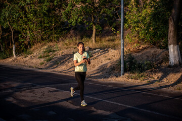 Obraz premium Slender girl in sportswear is jogging, holding smartphone in hands. Business woman talking on phone