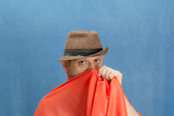 Bearded man wearing hat and covering part of his face with orange cloth.
