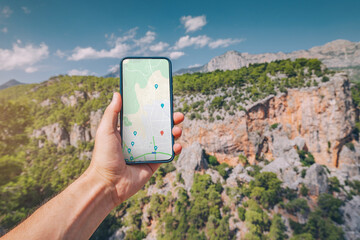 Young and sportive man on top of a mountain with a stunning view of canyon gorge in Turkey looks into a smartphone with a map app for navigation